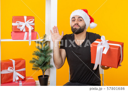 Young handsome man in a Santa Claus hat is holding congratulatory gifts next to a Christmas tree 57801686