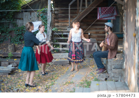 Company of people standing by the country house and talking - a man playing balalaika Company of people standing by the country house and talking - a man playing balalaika 57804473