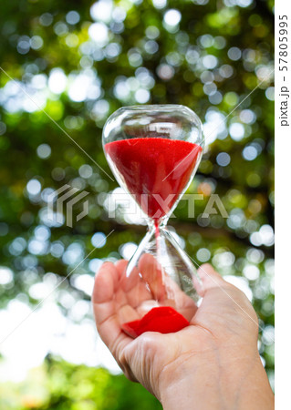 Woman's right hands holding red hourglass in bokeh green garden background, Close up & Macro shot, Selective focus, Time concept Woman's right hands holding red hourglass in bokeh green garden background, Close up & Macro shot, Selective focus, Time concept 57805995