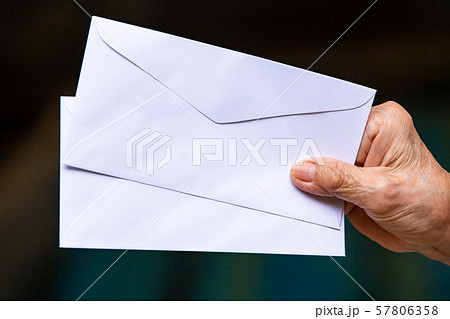 Senior woman's hand holding 2 white envelopes in black background, Close up shot, Business concept Senior woman's hand holding 2 white envelopes in black background, Close up shot, Business concept 57806358
