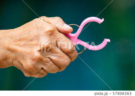 Senior woman's right hand squeezing pink plastic clothes peg in bokeh blue swimming pool background, Close up and Macro shot, Selective focus, Laundry concept Senior woman's right hand squeezing pink plastic clothes peg in bokeh blue swimming pool background, Close up and Macro shot, Selective focus, Laundry concept 57806363