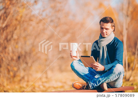 Young man drinking coffee with phone in autumn park outdoors 57809089