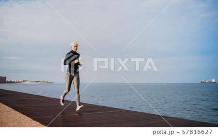 Side view of young sportswoman running outdoors on beach. Side view of young sportswoman running outdoors on beach. 57816627
