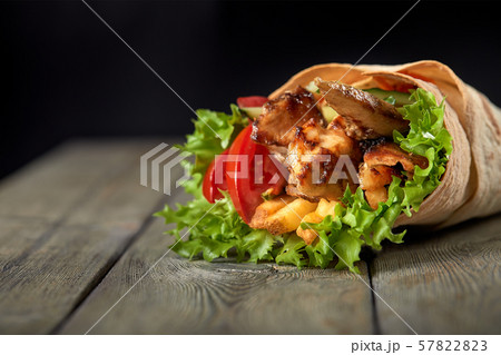 Shawarma rolled in lavash, moist grilled meat with onion, herbs and vegetables on wooden background. 57822823