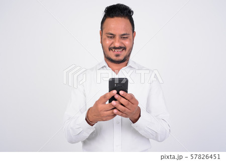 Studio shot of happy bearded Indian businessman using phone 57826451