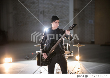 A musician man holding guitar and playing it on the background of a drum-kit 57842022