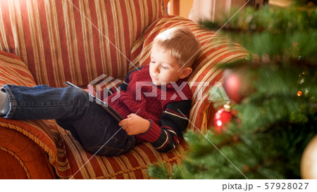 Portrait of smiling little boy lying on sofa next to beautiful Christmas tree in living room and Portrait of smiling little boy lying on sofa next to beautiful Christmas tree in living room and 57928027
