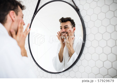 Young man looking in mirror in the bathroom in the morning, daily routine. 57929679
