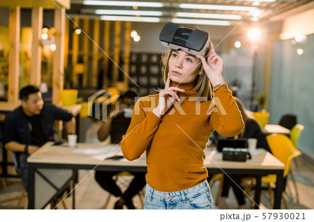 Pretty female business woman in orange sweater trying 3d vr glasses at work. Multiracial team of Pretty female business woman in orange sweater trying 3d vr glasses at work. Multiracial team of 57930021