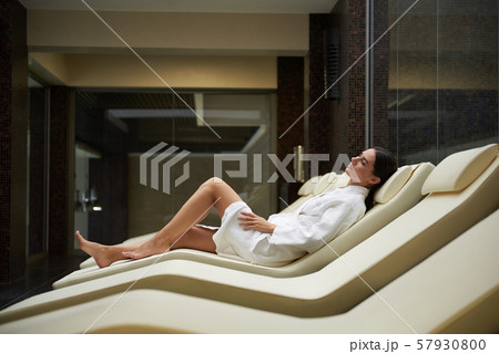 Attractive young woman in soft white bathrobe lying on comfortable daybed Attractive young woman in soft white bathrobe lying on comfortable daybed 57930800