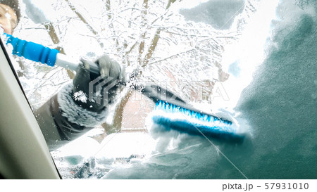 Close up image inside the snow covered car. Smiling lady clean up the windshield and wipers of her 57931010