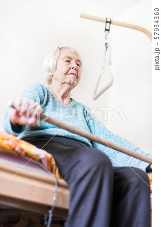 Elderly 96 years old woman exercising with a stick sitting on her bad. 57934360