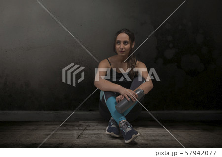 Female runner sitting legs crossed with water bottle on floor 57942077
