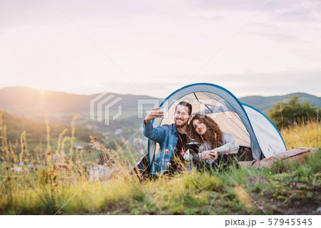 Young tourist couple travellers with tent shelter sitting in nature, taking selfie. Young tourist couple travellers with tent shelter sitting in nature, taking selfie. 57945545