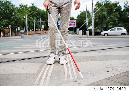 Midsection of young blind man with white cane walking across the street in city. Midsection of young blind man with white cane walking across the street in city. 57945666