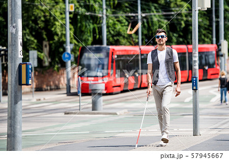 Young blind man with white cane walking across the street in city. Young blind man with white cane walking across the street in city. 57945667