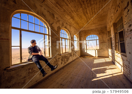 Tourist sits in a widow of a ruined house in Kolmanskop ghost town, Namibia 57949506