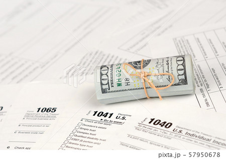 Tax forms lies near roll of hundred dollar bills. Tax forms lies near roll of hundred dollar bills. 57950678