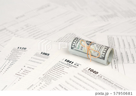 Tax forms lies near roll of hundred dollar bills. 57950681