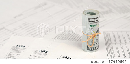 Tax forms lies near roll of hundred dollar bills. Tax forms lies near roll of hundred dollar bills. 57950692