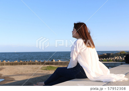 防波堤に座り海を眺める女性 57952308