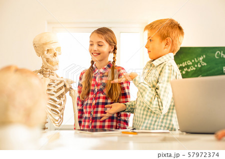 Pleased blonde kids looking at artificial skeleton 57972374