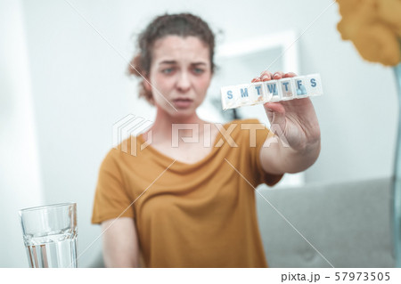 Curly red-haired woman wearing orange shirt holding pills Curly red-haired woman wearing orange shirt holding pills 57973505