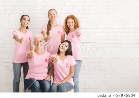 Volunteers In Breast Cancer T-Shirts Gesturing Thumbs-Up Over White Wall Volunteers In Breast Cancer T-Shirts Gesturing Thumbs-Up Over White Wall 57976904