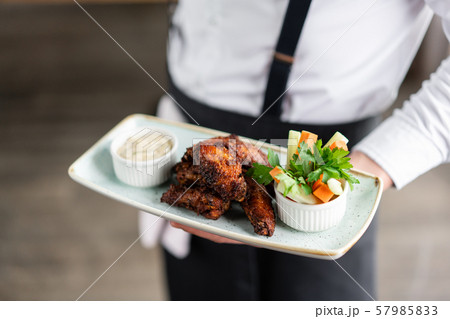 The waiter is holding a plate chicken wings grill. Barbecue restaurant menu, a series of photos of 57985833