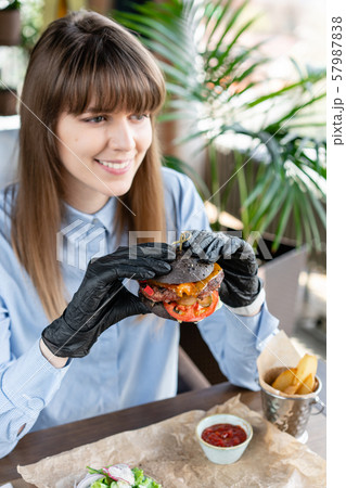 Young woman in blue shirt and black gloves eating delicious juicy hamburger with beef chop. Burgers Young woman in blue shirt and black gloves eating delicious juicy hamburger with beef chop. Burgers 57987838