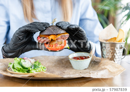 Young man in business suit and black gloves eating delicious juicy cheeseburger with beef chop Young man in business suit and black gloves eating delicious juicy cheeseburger with beef chop 57987839