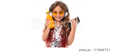 Smiling girl wearing glittery dress and yellow sunglasses, with big white earphones, listening to 57988751