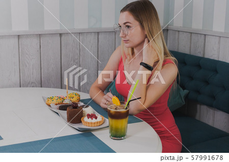 Girl sitting in a cafe with a plate of desserts. 57991678