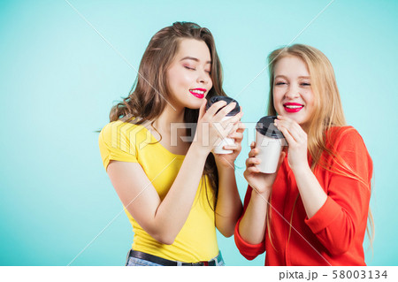 Two smiling girls have coffee time on blue Two smiling girls have coffee time on blue 58003134
