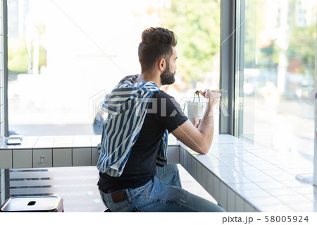 Portrait of a handsome man eating chinese noodles in a cafe and looking out the window. The concept Portrait of a handsome man eating chinese noodles in a cafe and looking out the window. The concept 58005924