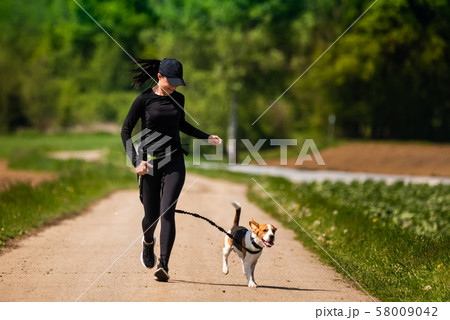 Sport girl is running with a dog (Beagle) on the 58009042