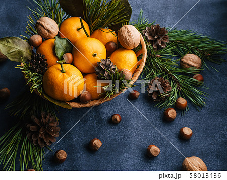 Hazelnuts, walnuts and tangerines decorated with Christmas branches and pine cones 58013436