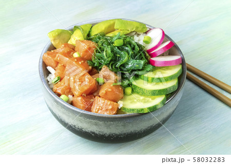 A bowl of salmon poke with avocado, wakame and cucumber on a teal blue background A bowl of salmon poke with avocado, wakame and cucumber on a teal blue background 58032283