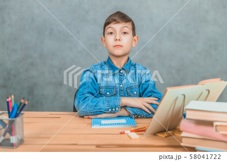 Smart serious schoolboy sitting with confident face expression, his hands folded on the desk. Smart serious schoolboy sitting with confident face expression, his hands folded on the desk. 58041722