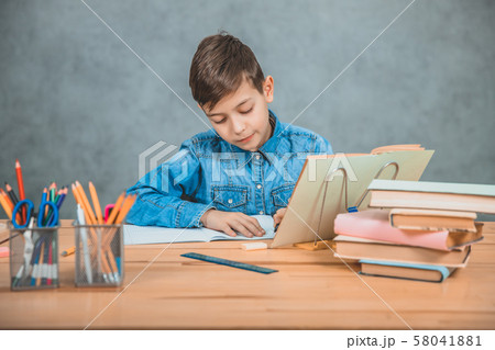 Young concentrated school kid in blue jeans t-shirt writing sitting at table with books. Young concentrated school kid in blue jeans t-shirt writing sitting at table with books. 58041881