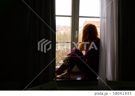 girl sitting on a windowsill and looking at the 58041935