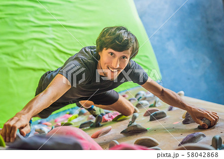 Muscular man practicing rock-climbing on a rock wall indoors 58042868