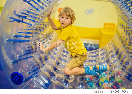 Cute little boy, playing in Zorb a rolling plastic cylinder ring with a hole in the middle, intdoor 58042987