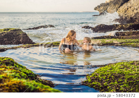 Mother and son tourists on Pantai Tegal Wangi Beach sitting in a bath of sea water, Bali Island Mother and son tourists on Pantai Tegal Wangi Beach sitting in a bath of sea water, Bali Island 58043372