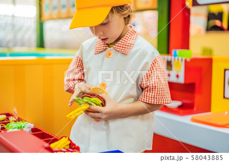 The boy plays in the toy kitchen, cooks a hamburger The boy plays in the toy kitchen, cooks a hamburger 58043885