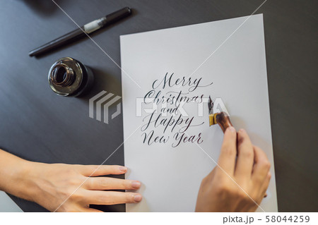 Merry christmas and a happy new year. Calligrapher Young Woman writes phrase on white paper 58044259