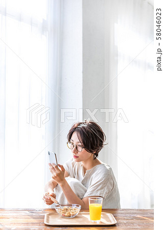 スマホを見ながら朝食を食べる女性 58046023