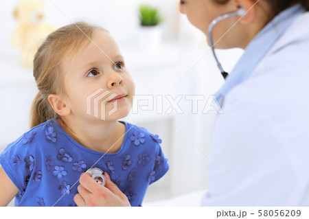 Doctor examining a little girl by stethoscope. Happy smiling child patient at usual medical 58056209