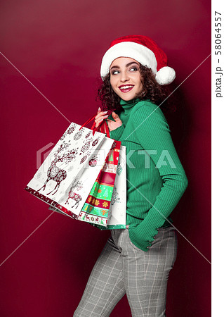 Beautiful fashion woman in santa claus hat. wearing bright Christmas carrying colorful shopping bags 58064557