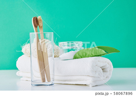 Wooden bamboo toothbrushes in glass, baking soda and towel on green background. Personal hygiene concept 58067896